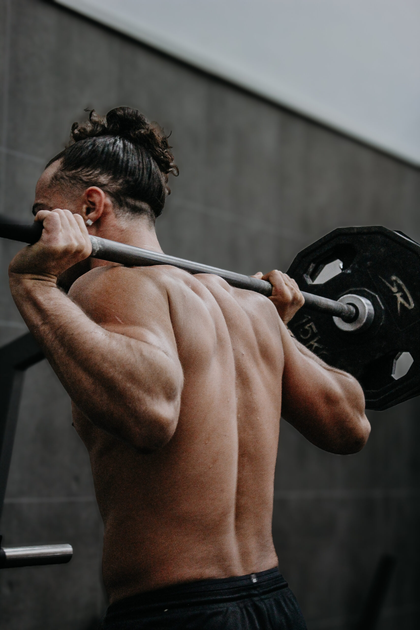 photo d'un homme de dos avec une barre de musculation sur les trapèzes